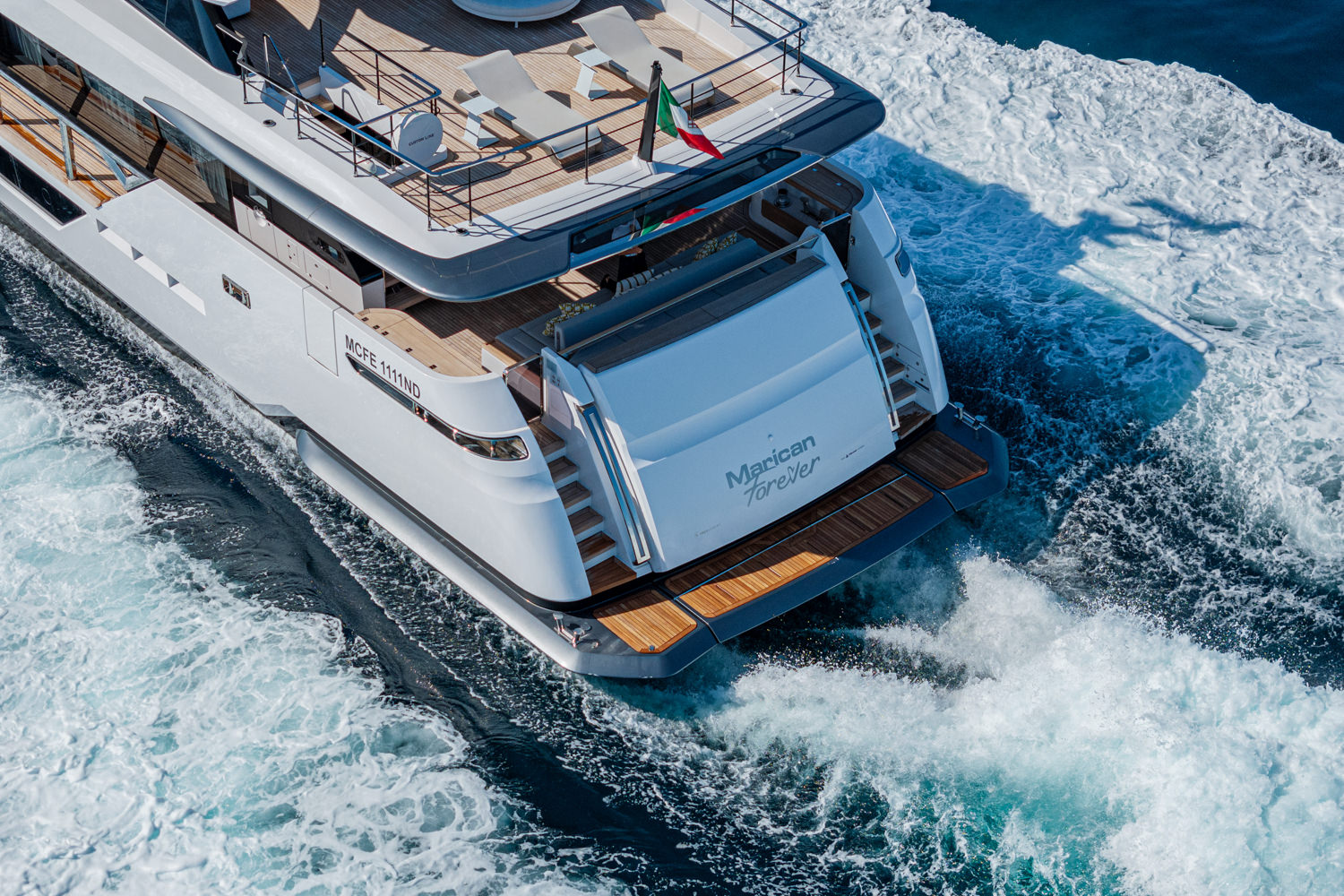 Aerial photograph of a yacht cruising near Monaco, with the beautiful Mediterranean coastline in the background.