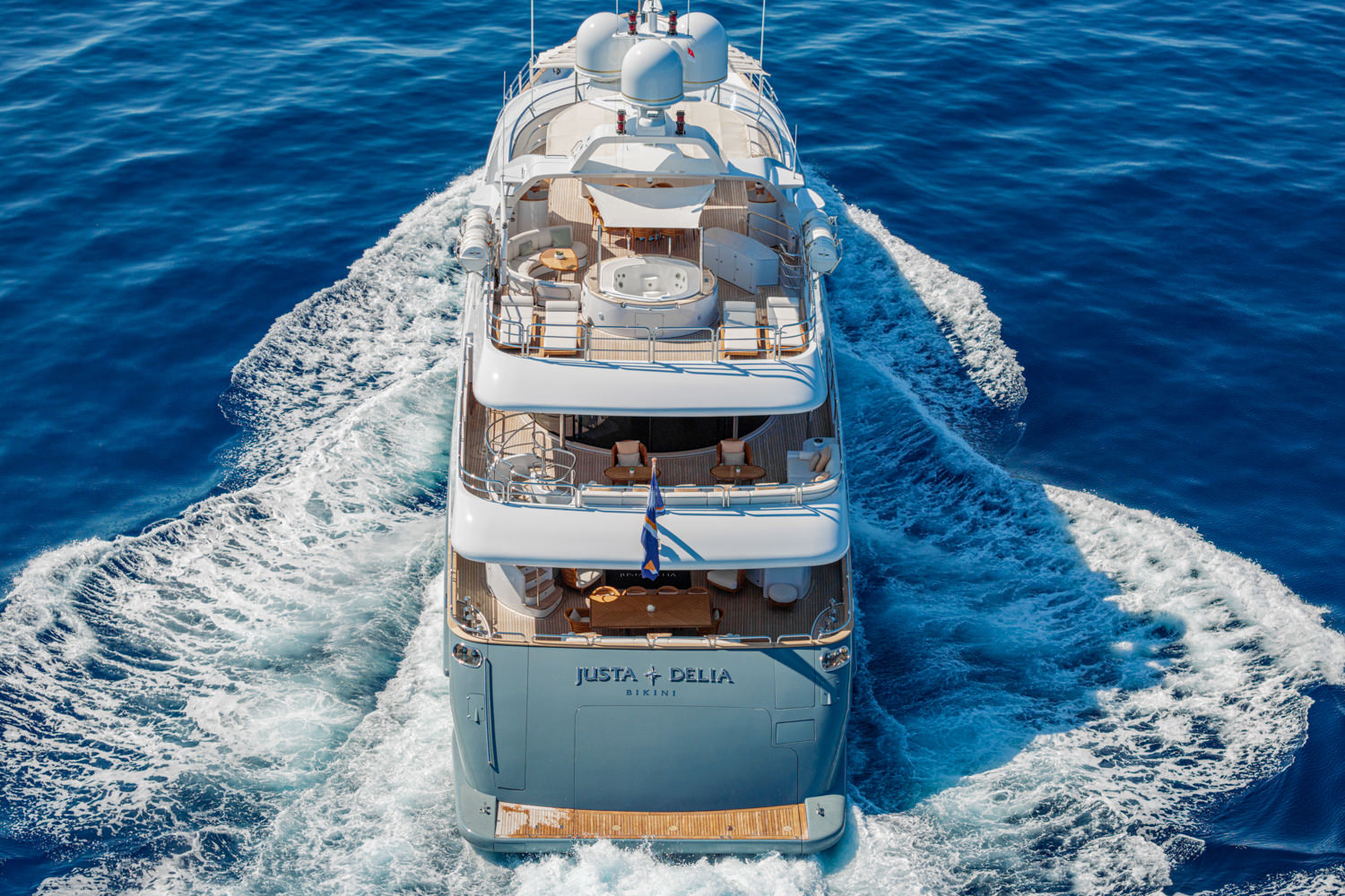 Aerial photograph of a yacht cruising near Monaco, with the Mediterranean Sea and coastline in the background.