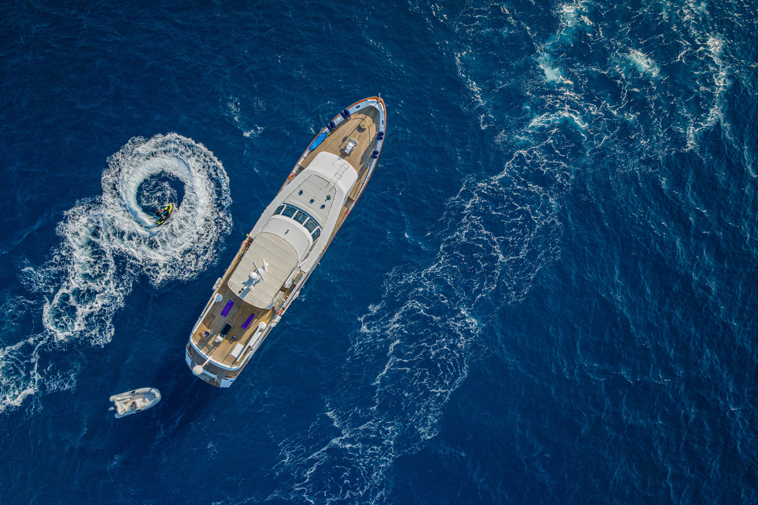Aerial view of a yacht cruising near Cannes, with the Mediterranean coastline and clear waters in the background.