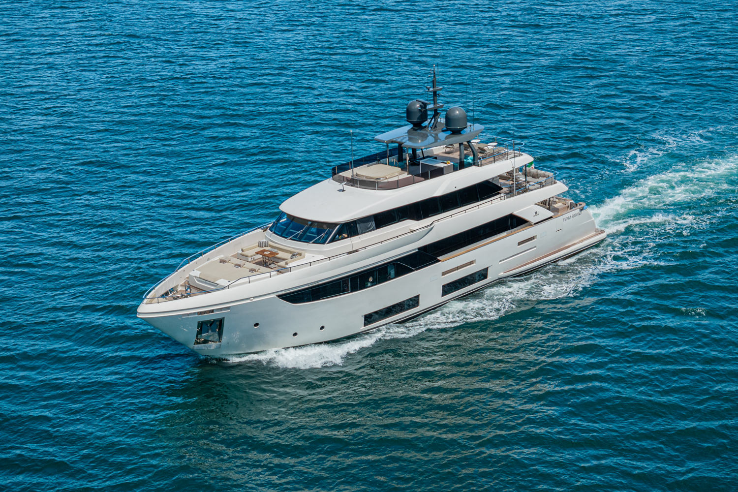 Aerial photograph of a yacht cruising near Antibes, with the Mediterranean coastline and clear blue waters in the background.