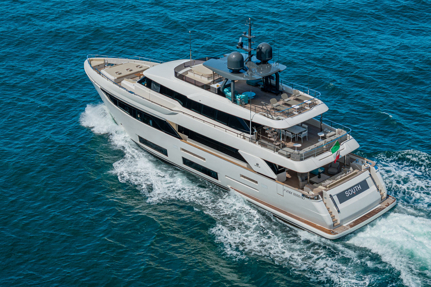 Aerial photograph of a yacht cruising near Saint-Tropez, with the Mediterranean coastline and clear waters in the background.