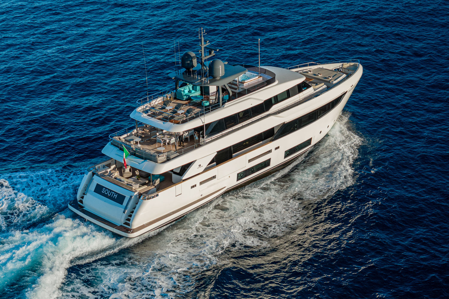 Aerial view of a yacht cruising along the Amalfi Coast, with steep cliffs and vibrant blue waters surrounding it.