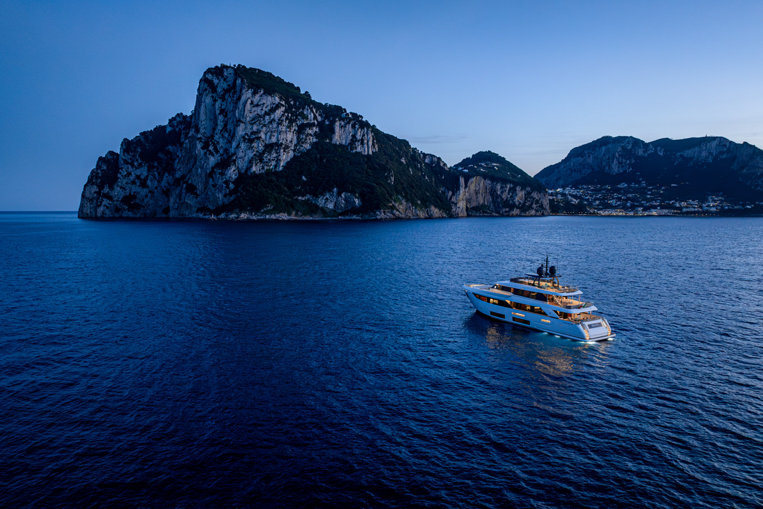 Aerial view of a yacht passing near the iconic cliffs of Capri, with the Mediterranean Sea stretching beyond.