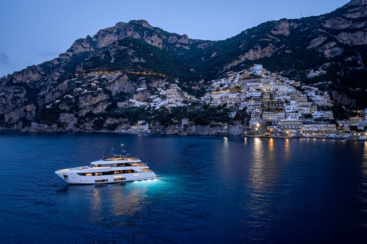 Aerial view of a yacht cruising near the Faraglioni rocks in Capri, with the beautiful Mediterranean coastline in the background.