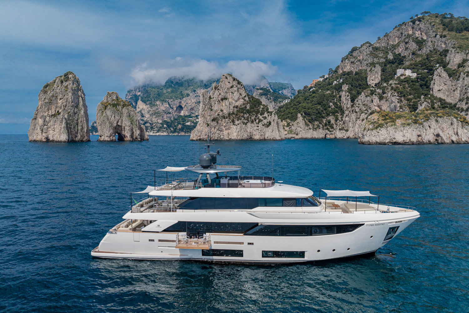 Aerial view of a yacht near the Faraglioni rocks in Capri, with crystal-clear waters and dramatic cliffs.