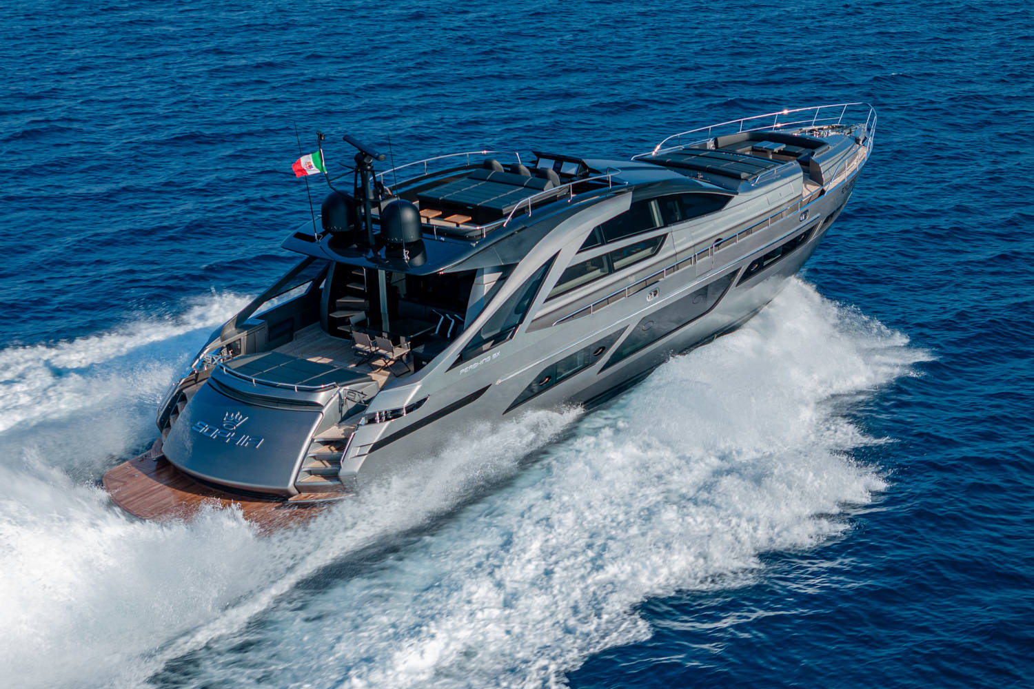 Aerial photograph of a yacht cruising near Monaco, with the Mediterranean coastline and clear waters in the background.