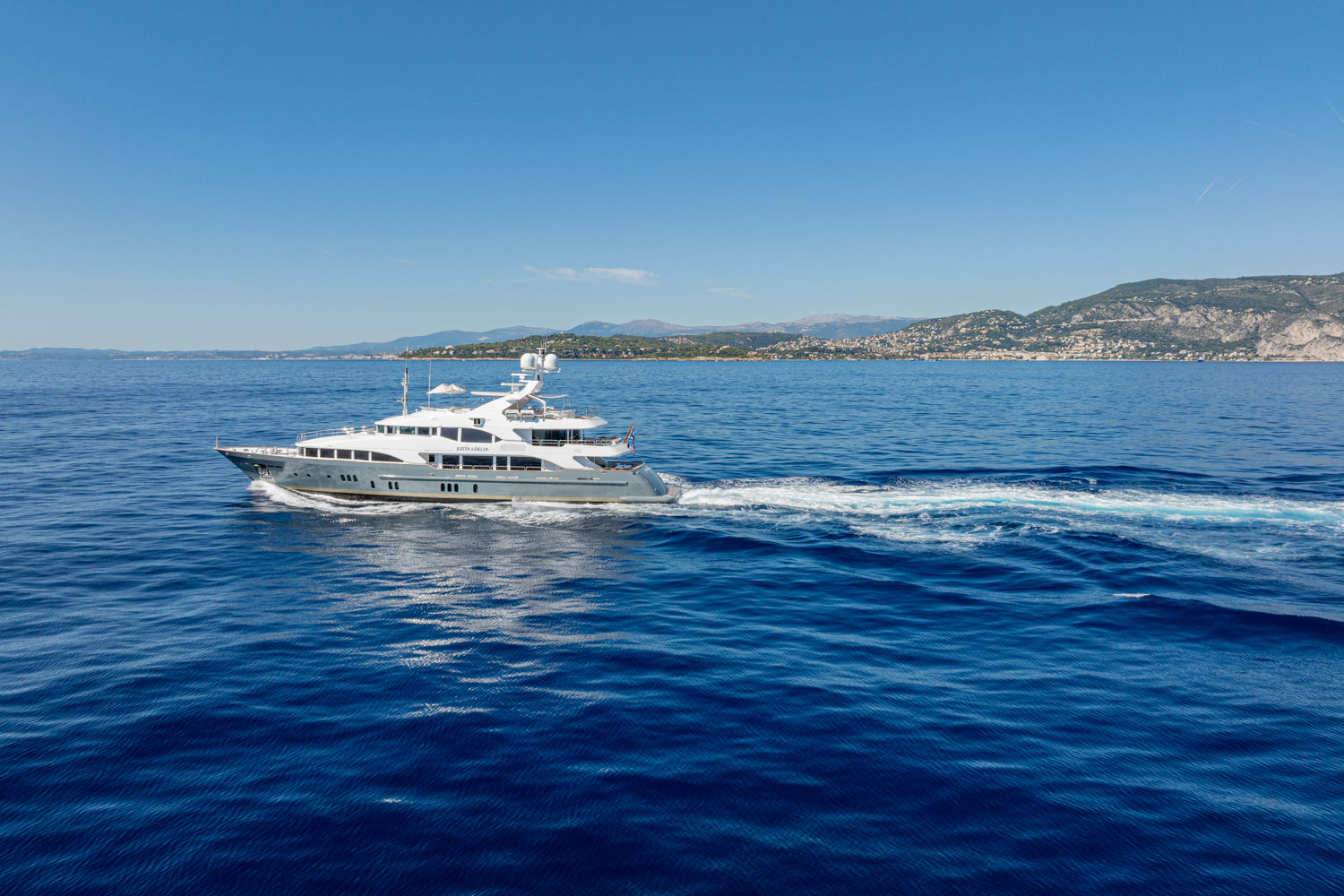 Aerial shot of a luxury yacht cruising near Cannes, with the Mediterranean coastline in the background.
