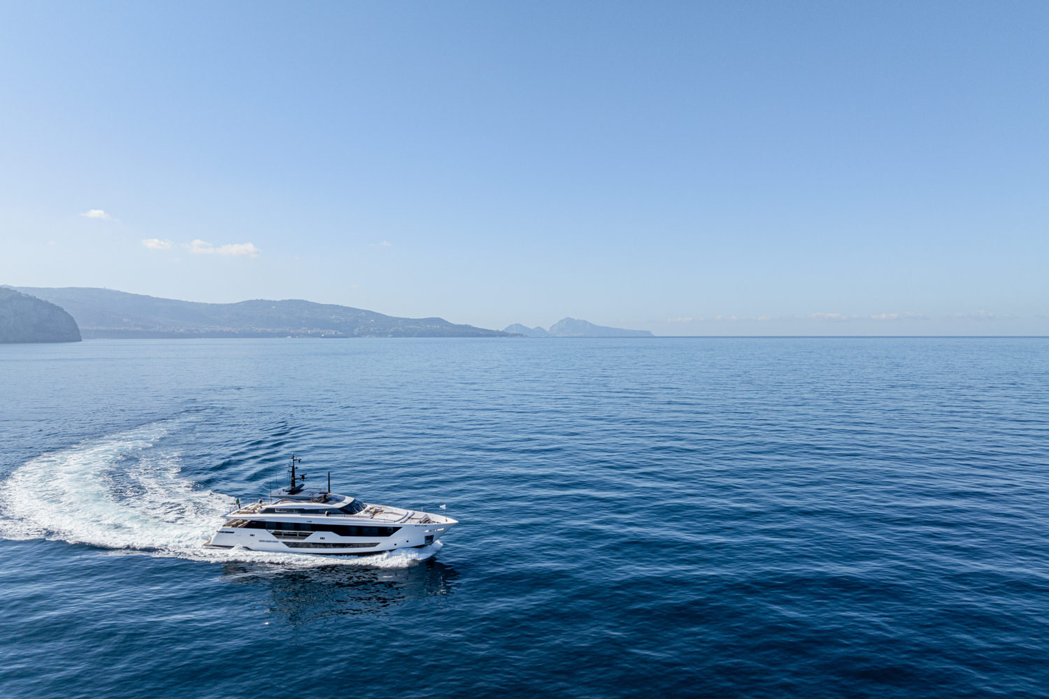 Aerial photograph of a yacht cruising near Cannes, with the Mediterranean coastline in the background.
