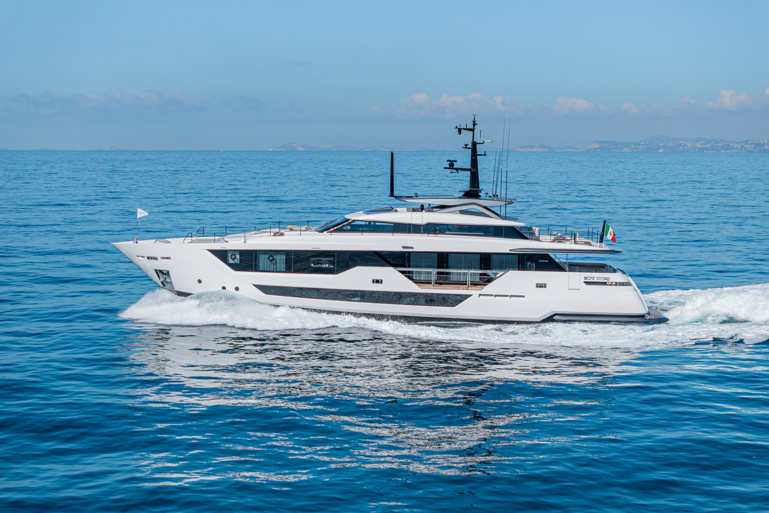 Aerial photograph of a luxury yacht cruising near Nice, with the Mediterranean coastline and cityscape in the background.