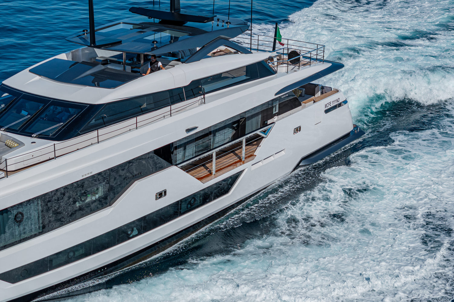Aerial view of a luxury yacht cruising near Monaco, with the Mediterranean Sea and coastline in the background.