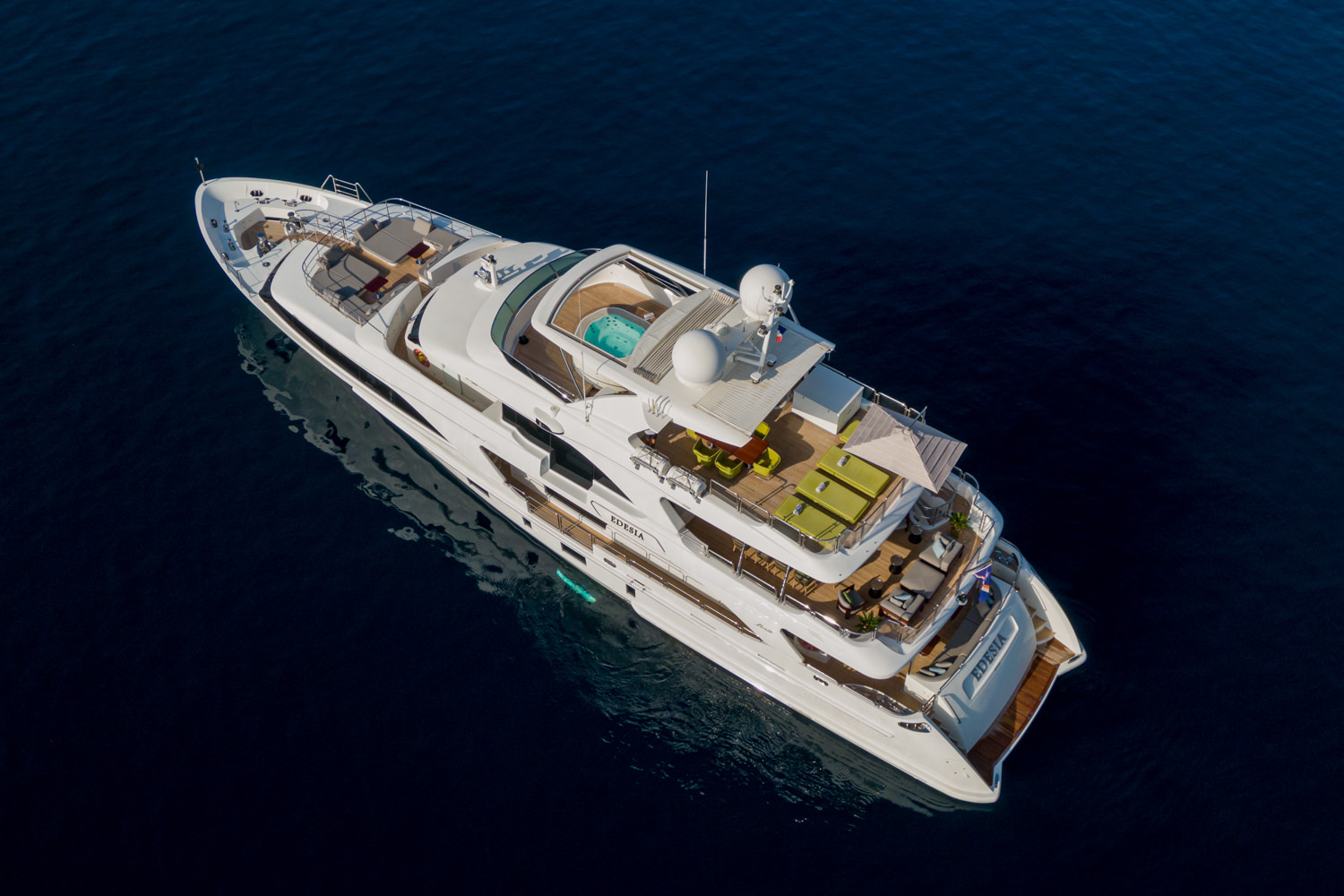 Aerial photograph of a luxury yacht cruising near Genoa, with the Ligurian coastline in the background.