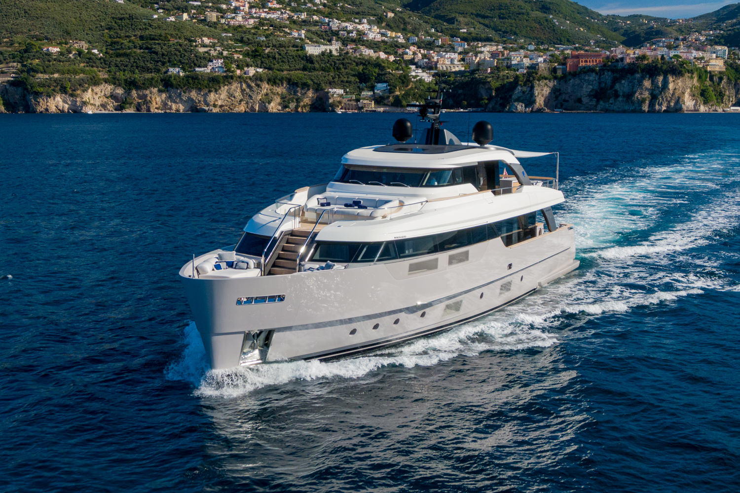 Drone image of a luxury yacht sailing near Monaco, with the Mediterranean coastline in the background.