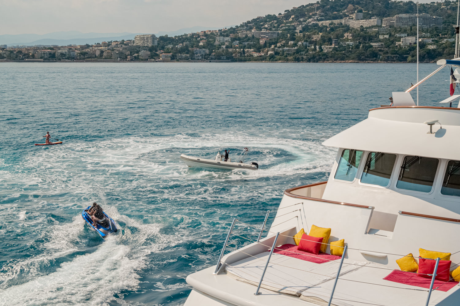 Aerial view of a luxury yacht cruising near Saint-Tropez, with the Mediterranean coast in the background.