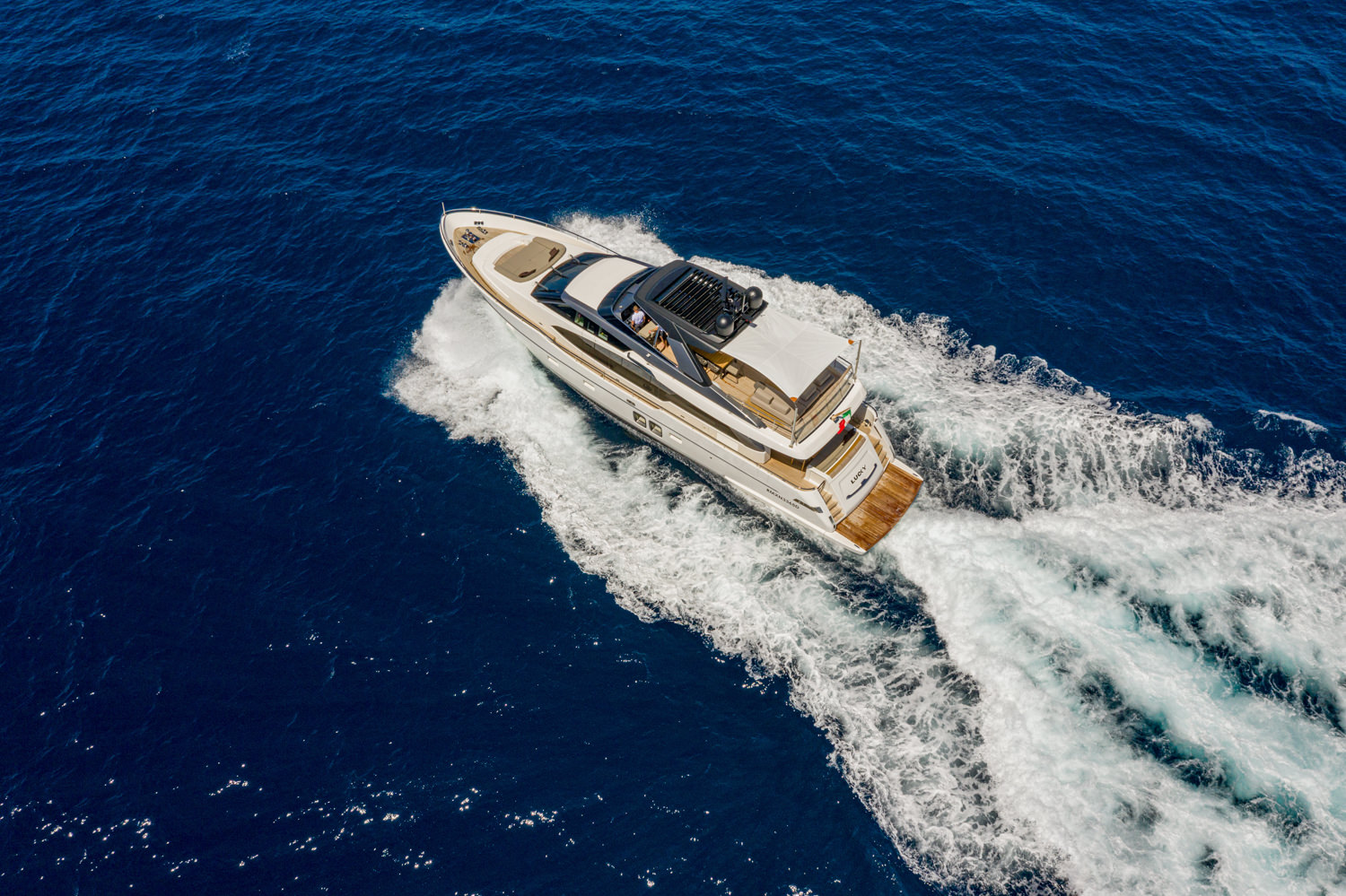 Drone image of a luxury yacht sailing near Genoa, with the Italian coastline in the background.