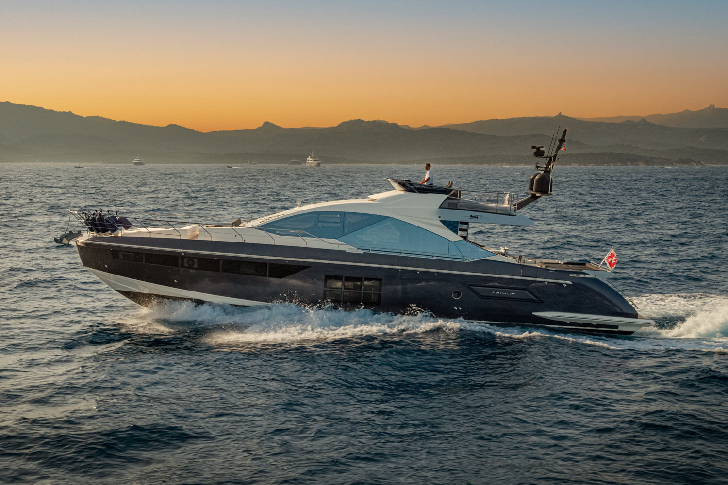 Aerial photograph of a luxury yacht sailing near Cannes, with the Mediterranean coastline in the background.