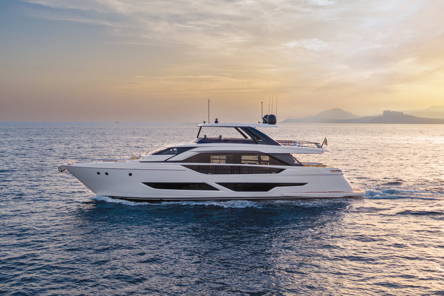 Aerial photograph of a luxury yacht cruising near Saint-Tropez, with the French Riviera coastline in the background.