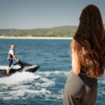 A guest aboard a yacht watches someone riding a jet ski during a water sports activity at sea.